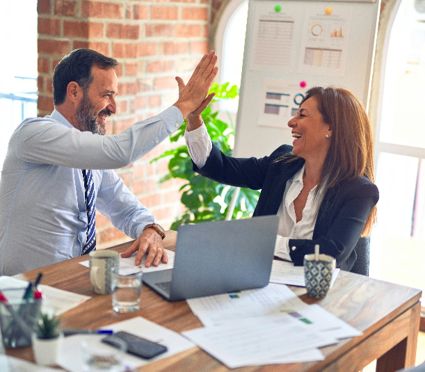 Two smiling professionals high-five at a desk, celebrating success—reflecting Revenue Nomad’s role in driving growth.